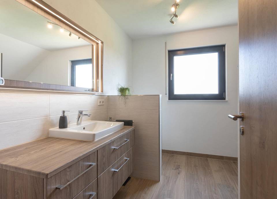 Das moderne Design des individuellen Fertighauses in Jesberg wird auch im Badezimmer spürbar. Hell und einladend bietet das Bad alles was man braucht.