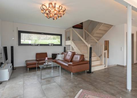 Vom Wohnbereich des großzügigen Einfamilienhauses führt eine helle Holztreppe ins obere Geschoss. Sie unterstützt die freundliche Atmosphäre des Raumes. 