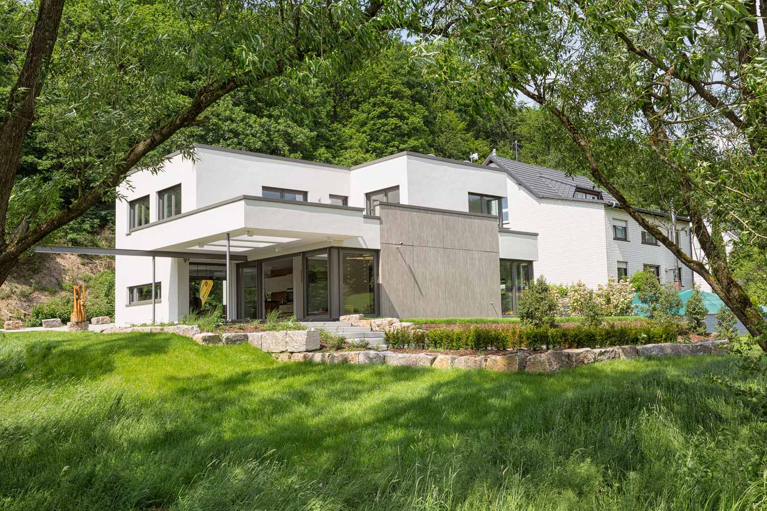 Das Plusenergiehaus Satchmo ist ein Musterhaus von Büdenbender Hausbau in Netphen-Hainchen. Der weiße Putz verschmilzt mit der Holzoptik zu einem einmaligen Gesamtbild. Die überdachte Terrasse ist nur eines des vielen Highlights, die das Haus zu bieten hat.